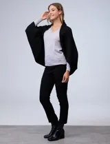 Cardigan negro de tejido suave, estilo poncho o capa, con cuello tipo chal y mangas amplias.