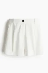 Short blanco de corte sastrero con cierre y botón, bolsillos al bies y bolsillo trasero decorativo. Piernas con pinzas y pliegues adelante y atrás.
