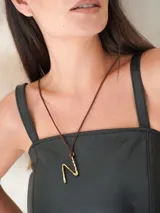 Gargantilla marrón de cuero con dije de bronce en forma de letra M.