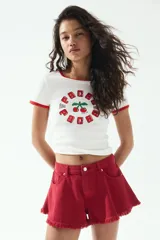 Remera blanca de algodón con cuello y mangas con ribete rojo. Estampado con cerezas y texto "Ibiza" en rojo.