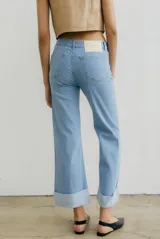 Pantalón de jean azul oscuro con corte acampanado, tiro medio y dobladillo en el ruedo. Presenta costuras marcadas en el frente y estampado abstracto en tonos grises y blancos en el interior del dobladillo.