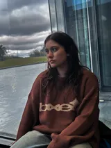 Sweater marrón de tejido de punto con cuello redondo y mangas largas. Presenta un diseño gráfico en color beige en el frente.