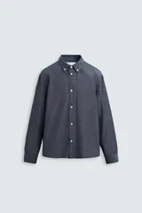 Camisa azul de algodón con textura chambray, corte regular fit, cuello abotonado, manga larga con puños abotonados, bolsillo de parche en el pecho y cierre frontal con botones.