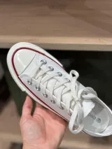 Zapatillas bajas de lona color blanco, con cordones marrones, puntera de goma y base blanca.