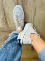 Zapatillas bajas de lona color blanco, con cordones marrones, puntera de goma y base blanca.