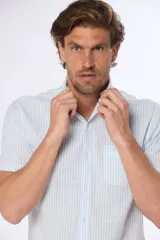 Camisa celeste y blanca a rayas verticales, de lino y algodón, manga corta, corte slim fit, con cuello abotonado y bolsillo en el pecho.