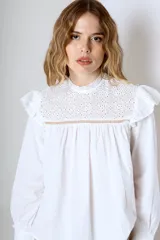 Blusa blanca de mangas largas con cuello alto con volados y detalles de encaje.