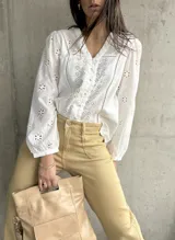 Camisa blanca de algodón con bordado inglés, cuello en V y mangas largas abullonadas.