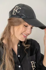 Gorra de béisbol negra, confeccionada en cuero, con visera curva y bordado frontal de monograma "PEC" en hilo color beige.