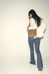 Pantalón de jean azul de tiro alto con nervio marcado delantero, bolsillos delanteros y traseros, bajo acampanado y cierre frontal con cremallera y botón.
