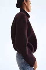 Campera corta de tejido efecto neopreno color marrón oscuro o ciruela, con cuello chimenea alto y cierre frontal metálico. Presenta hombros caídos y un bajo fruncido con elástico que le da un calce holgado.