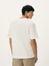 Camiseta blanca de algodón con cuello redondo y mangas cortas. Estampa rectangular con borde negro que contiene la frase "NATURAL ATMOSPHERE" en letras mayúsculas y una imagen de montañas y mar.