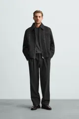 Sobrecamisa negra con textura de tejido bouclé y rayas verticales plateadas. Tiene cuello solapa, manga larga con puños abotonados, bolsillos laterales y cierre frontal con cremallera.