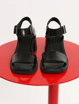 Sandalias negras de charol con taco bloque y pulsera al tobillo con hebilla metálica.