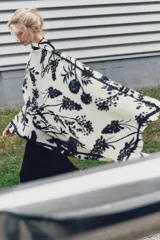 Pañuelo rectangular de color crema con estampado de ramas y flores en negro. Tiene terminaciones deshilachadas.