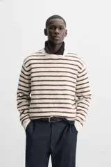 Sweater de punto color crudo con rayas horizontales marrones, de corte relaxed fit, cuello redondo y mangas largas con terminaciones en rib.