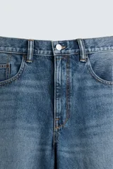 Bermuda de denim de algodón, color gris claro lavado, de corte ancho (baggy fit) y largo hasta la rodilla. Presenta cinco bolsillos y cierre frontal con cremallera y botón.