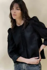 Blusa de lino blanca con escote a la base y terminación de voladito al bies desflecado. Delantera con alforzas verticales y mangas románticas tres cuartos, con detalle de puntilla. Puños con alforzas y voladitos que suman un toque femenino. Espalda abotonada.