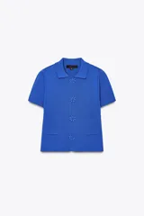 Chaqueta de punto azul con cuello solapa y manga corta. Tiene bolsillos delanteros de parche y cierre frontal con botones grandes con abalorios.