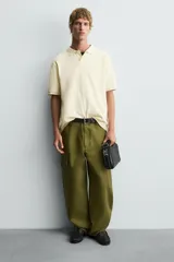 Bandolera negra con textura grabada, compartimento principal con cierre de cremallera, bolsillo interior con cremallera, bolsillo trasero con cremallera y asa de hombro ajustable.