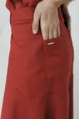 Falda midi color ladrillo, de corte evasé y tiro alto, con bolsillos laterales y botón decorativo en la cintura.