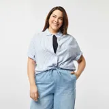 Camisa celeste y blanca a rayas verticales, de corte holgado y mangas cortas con dobladillo.