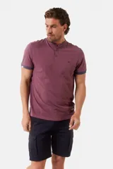 Remera de manga corta color azul grisáceo con cuello mao y tapeta de botones. Los puños de las mangas y el cuello son de color azul marino contrastante. Presenta un pequeño logo bordado en el pecho.