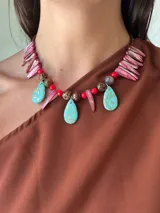 Collar artesanal con cuentas de cristal checo, piedras facetadas y colgantes en forma de lágrima turquesa con detalles dorados. Incluye elementos decorativos en forma de colmillo teñido de rosa y cuentas redondas marrones.