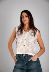 Chaleco sin mangas de tela blanca con bordados florales en hilo azul y blanco, con cierre frontal de botones.