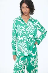 Camisa de manga larga verde con estampado de hojas blancas. Tiene cuello clásico, cierre con botones y puños con botón.