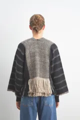 Chaqueta peplum tejida a rayas horizontales negras y grises, con mangas anchas y detalle de flecos en el ruedo.