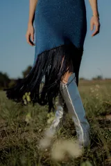 Vestido corto tejido en lurex con diseño geométrico en cuero en el frente, breteles de cuero intervenido a mano con tientos de cuero plateado y terminación en flecos.