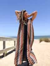 Vestido largo tejido con patrón geométrico en tonos marrón, beige, blanco y negro. Tiene escote en V y corte holgado.