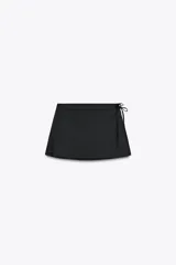 Falda pantalón negra de tiro alto con aberturas laterales y cierre cruzado con lazadas y cremallera oculta.