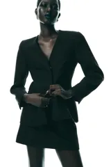 Blazer negra entallada, de escote pico y manga larga con hombreras. Tiene bolsillos delanteros de vivo y cierre frontal con botones a presión ocultos.