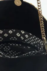 Cartera de mano negra de cuero gamuzado con solapa bordada con diseño de alas en tonos dorados y plateados. Tiene cierre magnético, bolsillos internos y cadena metálica dorada vieja.