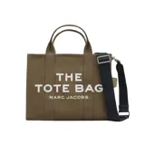 Bolso tote mediano de lona color verde oliva, con asas superiores y correa larga tejida ajustable y desmontable de color negro. Presenta el logo estampado en blanco en el frente: "THE TOTE BAG MARC JACOBS".