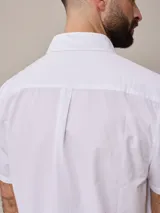 Camisa de algodón blanca de manga corta, con cuello abotonado y botones frontales.
