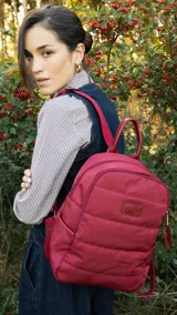 Mochila capitoneada color bordó de nylon, con apertura superior con cierre y tiradores metálicos, bolsillos internos, bolsillo con cierre metálico al frente, correa corta de mano y correas de galón regulables para colgar en la espalda.