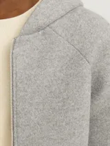 Campera gris melange con capucha, cierre frontal con cremallera, bolsillos laterales y puños elásticos.