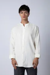 Camisa de lino color blanco roto, de manga larga y corte recto, con cuello mao y cierre frontal de botones.