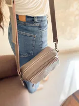 Bandolera color visón, fabricada en cuero con forro de tela. Tiene bolsillo interior y exterior. Entra billetera grande.