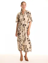 Vestido maxi de crepe color beige con estampado floral en tonos marrones y negros. Presenta cuello a la base, escote en V, abertura central con botones y cintura con lazo de ajuste y hebilla.