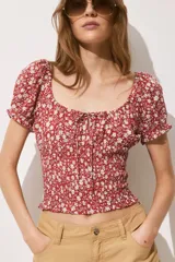 Blusa roja con estampado de flores blancas, escote cuadrado con cordón ajustable, mangas cortas abullonadas con elástico en hombros y puños, cintura fruncida y volados en mangas y bajo.