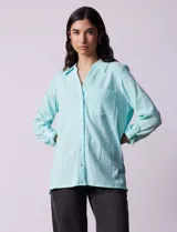 Camisa celeste texturada con cuello con solapa y abertura central con botones. Delantera con bolsillo aplicado y largo de manga regulable con presilla y botón.