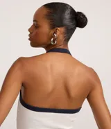 Top de tejido rib blanco, ajustado al cuerpo, con escote profundo y cuello halter. Presenta un ribete contrastante azul marino en el escote y a lo largo del cierre frontal de botones.