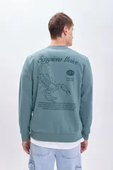 Sudadera verde con cuello redondo y mangas largas. Estampado en la espalda con la frase "Scorpions thrive", un escorpión, el número 073 y un texto descriptivo.