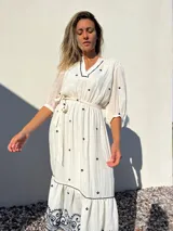 Vestido largo blanco con bordados azules, escote en V, mangas 3/4 abullonadas y lazo en la cintura.