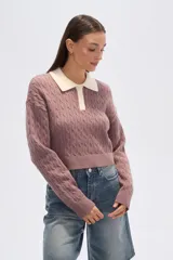 Sweater de tejido de punto con trenzas, color malva/rosado, de corte cropped y manga larga. Presenta cuello polo con solapas en color crema y cierre frontal de botones.