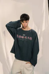 Crewneck (jersey de cuello redondo) unisex color gris oscuro, con estampado frontal que dice "RE:SKIN" y texto pequeño debajo. Presenta mangas largas y corte holgado.